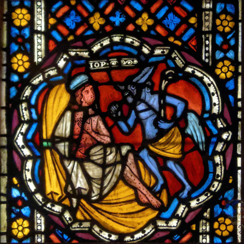A stained glass window of Job and the Devil, the Devil has blue skin